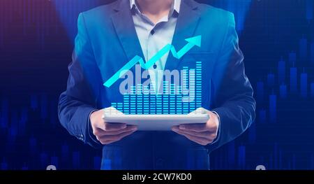 Businessman Holding Digital Tablet With Increasing Financial Graph, Blue Background Stock Photo