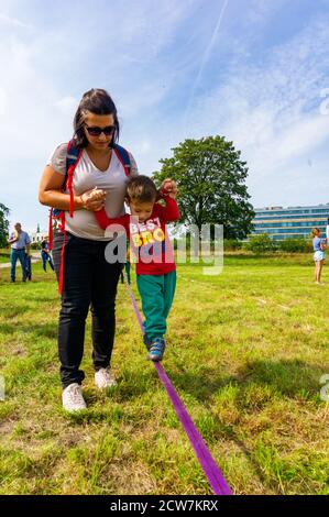POZNAN, POLAND - Sep 13, 2020: Woman helping a boy balancing on a rope at a grass field during the Aktywna Warta event. Stock Photo