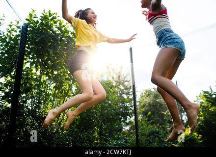 Low angle view of young teenager girls friends outdoors in garden, jumping on trampoline.