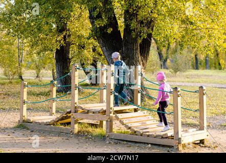 Wooden play bridge for children, located in the Park among the trees. Outdoor playgrounds. A bridge made of wooden planks with a rope railing, where s Stock Photo