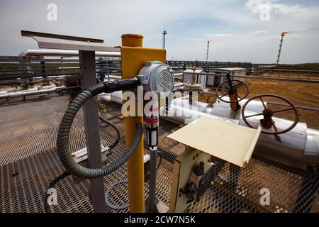 Oil refinery plant. Pipes, valves and gauge meters. Gas torch on grey sky background. Focus on foreground. Zhaik-Munai oil deposit, Kazakhstan. Stock Photo