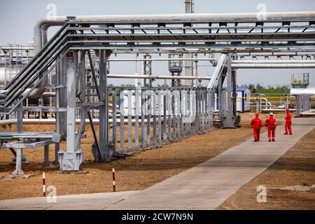 Oil refinery and gas processing plant. Three oil workers in red work wear and helmets under pipelines. Zhaik-Munai oil deposit, Kazakhstan. Stock Photo