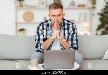 Pensive young man sitting at table, using computer Stock Photo