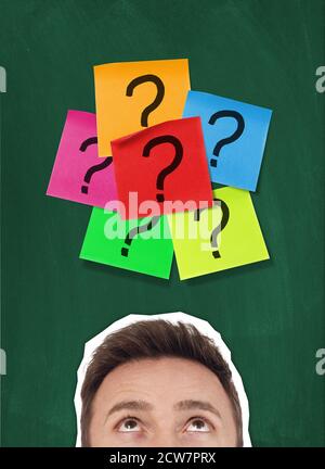 Man looking at adhesive notes with question marks on blackboard Stock Photo