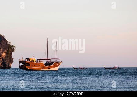 Sailing wooden ship in the old style sails on the sea. Nearby there are two small long-haul boats. Stock Photo