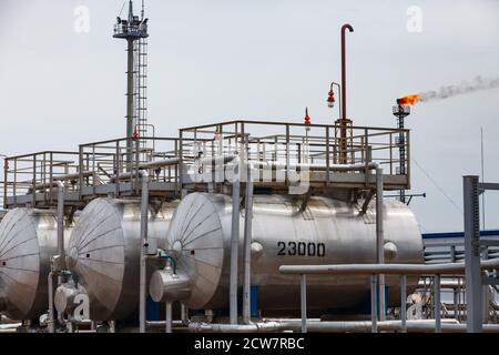 Oil refinery plant. Heat exchangers, lighting mast, platforms and orange gas torch on grey sky background. Zhaik-Munai oil deposit, Kazakhstan. Stock Photo