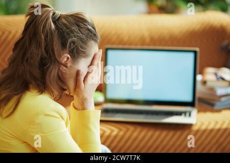 stressed elegant 40 years old woman in yellow jacket in the modern house in sunny day near laptop blank screen. Stock Photo