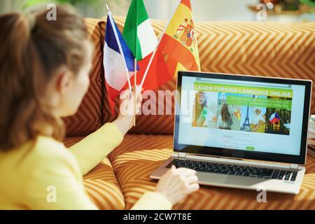 Seen from behind woman with flags learning foreign language online on a laptop in the house in sunny day. Stock Photo