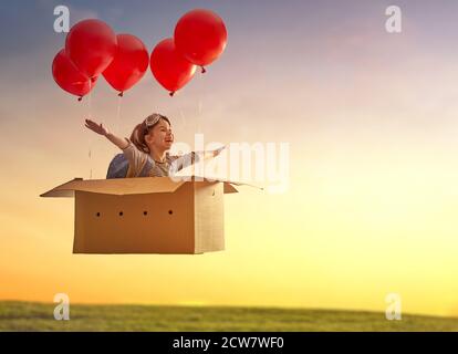 Dreams of travel! Child is flying in cardboard box with air balloons. Stock Photo