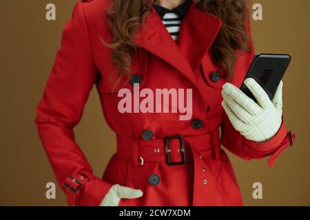 Life during coronavirus pandemic. Closeup on female in red coat sending text message using smartphone on bronze background. Stock Photo