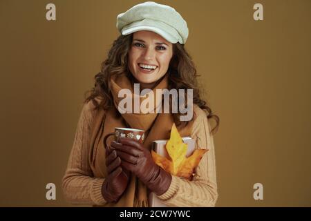 Hello september. Portrait of happy modern female in scarf with yellow autumn maple leaf, book, leather gloves and cup against beige background.