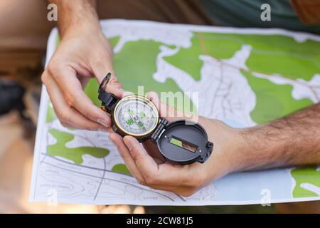Close up of unrecognizable man holding compass over map while looking for route during hike, copy space Stock Photo