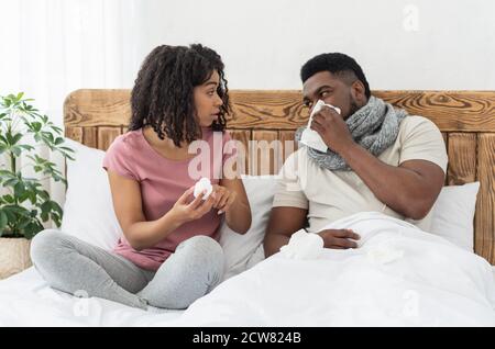 Sick african american man wrapped in scarf sitting in bed Stock Photo
