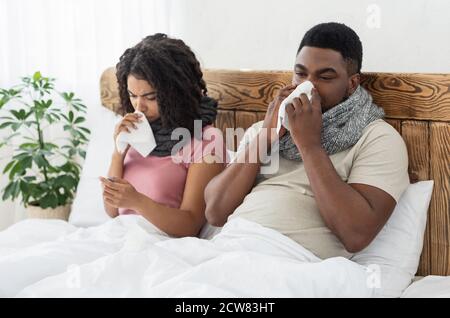 Ill african american couple wrapped in scarfs sitting in bed Stock Photo
