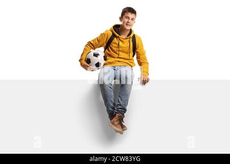 Teenager boy holding a soccer ball and sitting on a white panel board isolated on white background Stock Photo
