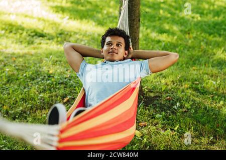 Young confident man with hands behind head relaxing in hammock Stock Photo