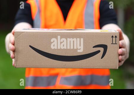 A man delivering an Amazon box with the Amazon smile logo in the UK Stock Photo