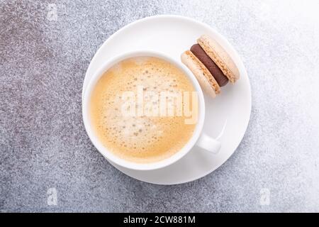 Close-up of cup with coffee and chocolate macaron on white plate. Concept of coffee break, top view - Image Stock Photo