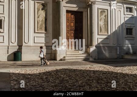 An elderly woman with a protective mask is walking home. Lights and shadows during the coronavirus epidemic in Italy. Stock Photo