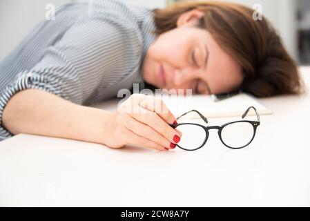 Tired female worker asleep at her desk with glasses still in her hand. Stock Photo