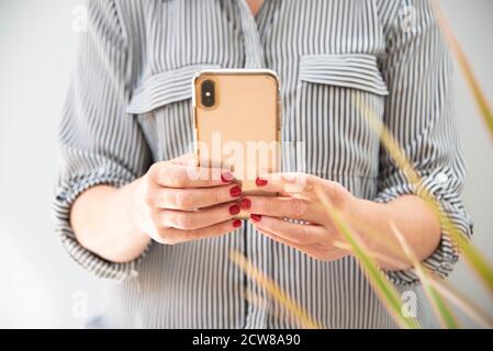 Cropped image of woman in smart shirt using smart phone indoors Stock Photo