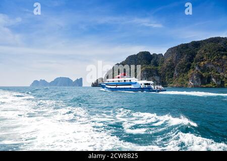 Blue with white and red accents pleasure speed boat. Sailing on the sea against a tropical island. Rear view. Motor track and waves on the water. Stock Photo