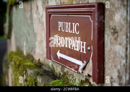 Close up view of an old distressed Public Footpath sign on a moss covered old stone wall. Stock Photo