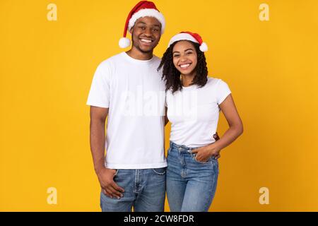 Joyful African Couple In Santa Christmas Hats Posing, Yellow Background Stock Photo