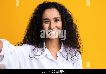 Happy beautiful brunette woman taking selfie over yellow studio background Stock Photo