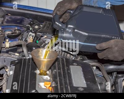 Mechanic topping up the oil in a car pouring a pint of oil through a funnel into the engine, close up of his hands and the oil Stock Photo