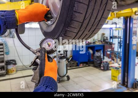Closeup of mechanic wearing orange gloves and blue outfit at repair service station checking tyre pressure with gauge. Stock Photo