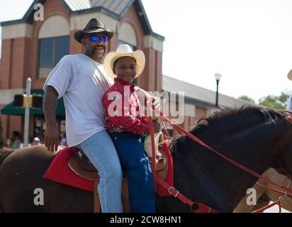 Bastrop, TX June 21, 2008: African-American cowboy and his son riding in a Juneteenth celebration in the historically African-American suburb of Bastrop, outside Austin. Juneteenth celebrates the day, June 19, 1865 when Union soldiers landed in Galveston, TX announcing the end of slavery and the Civil War.      ©Bob Daemmrich/ Stock Photo