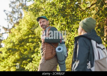 Portrait of happy father and son hiking together and talking while walking in forest with backpack, copy space Stock Photo