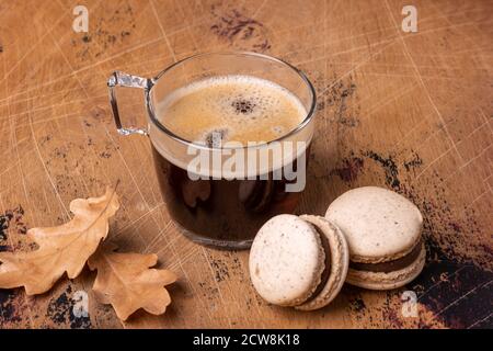 Glass cup of coffee and chocolate macarons on wooden background. Cozy autumn composition - Image Stock Photo