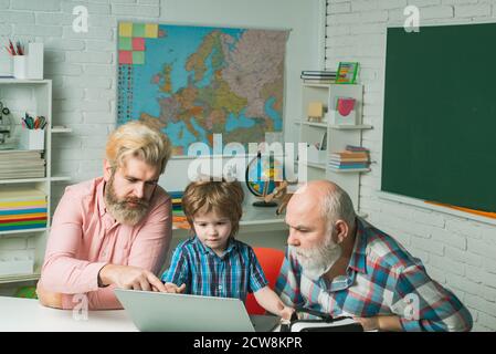 Generation of people and stages of growing up. Senior man using a laptop computer with his son and grandson. Cute little boy studying. Elementary Stock Photo