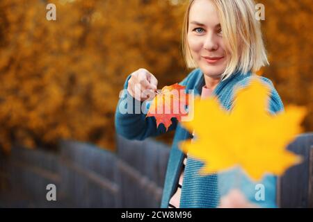Happy smiling blonde female holding maple leaves in both hands. Woman autumn outdoor portrait Stock Photo