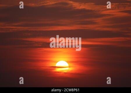 Sunset on colorful dramatic sky, orange sun shines through the clouds. Picturesque landscape for background Stock Photo