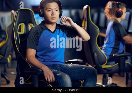Failure. Portrait of asian guy, male cyber sport gamer wearing headphones looking at PC screen with confused face while playing online video games. Participating in eSports tournament Stock Photo