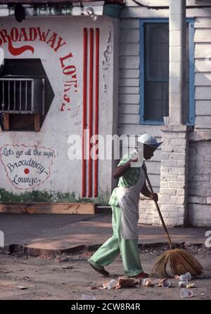 AFRICAN AMERICAN SWEEPING OUTSIDE CLUB, DOWNTOWN SAVANNAH, GEORGIA, USA, 1980s Stock Photo