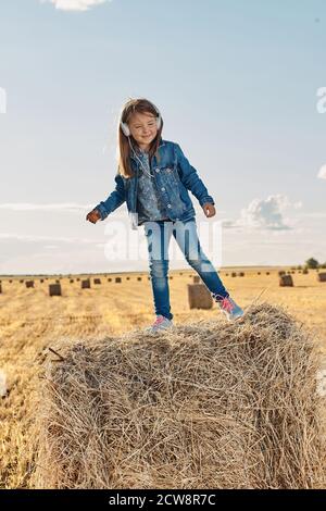 A cute little girl listens to music and dances on a haystack. High quality photo Stock Photo