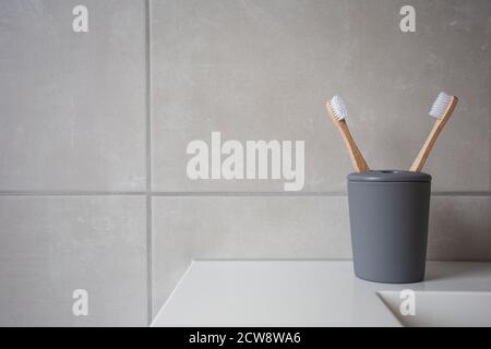 Eco Friendly bamboo natural organic toothbrushes in grey holder, with natural colored stone tiles bathroom wall background texture Stock Photo