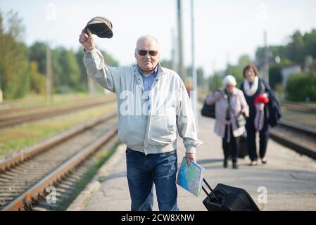 Portrait of senior elderly man holding hat and map,waiting for train on traveling journey during pandemic Stock Photo