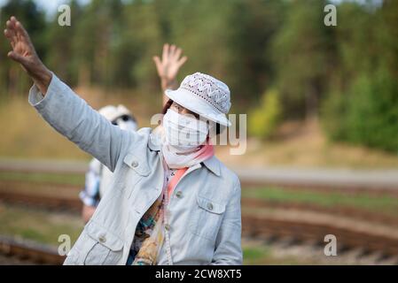 Elderly senior woman in a face medical mask with a hand raised to greet Stock Photo