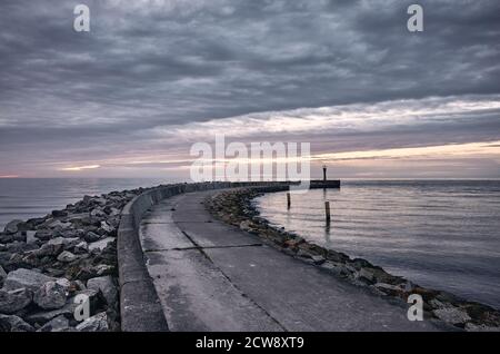 Rocky pier at sunset with dark sky, color toning applied. Stock Photo