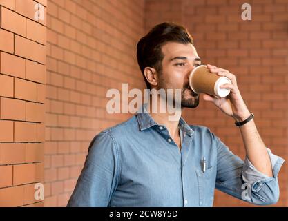 Portrait of middle east caucasian businessman drinking coffee from takeout disposable coffee cup and clipboard in meeting room after lunch break. Stock Photo
