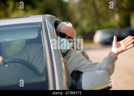 Senior man wearing anti virus mask are driving in a car during the COVID-19 pandemic Stock Photo