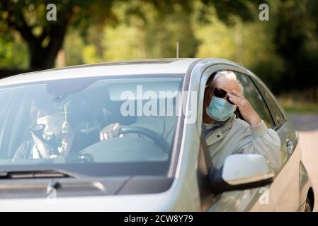 Senior couple wearing anti virus masks are driving in a car during the COVID-19 pandemic Stock Photo