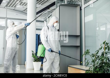 Fight against virus and protection of workers health. People in protective suits, masks and goggles, disinfects room with chemicals Stock Photo