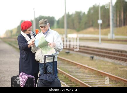 Happy senior elderly couple with suitcases looking at the map and waiting for the train to go on a trip Stock Photo