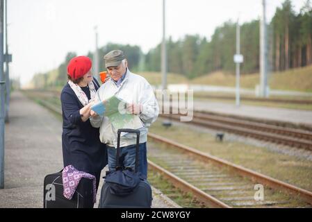 happy senior couple with suitcases looking at the map and waiting for the train to go on a trip Stock Photo
